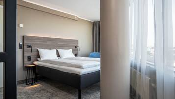 A modern hotel room with a bed, bedside tables, a chair, and a large window.