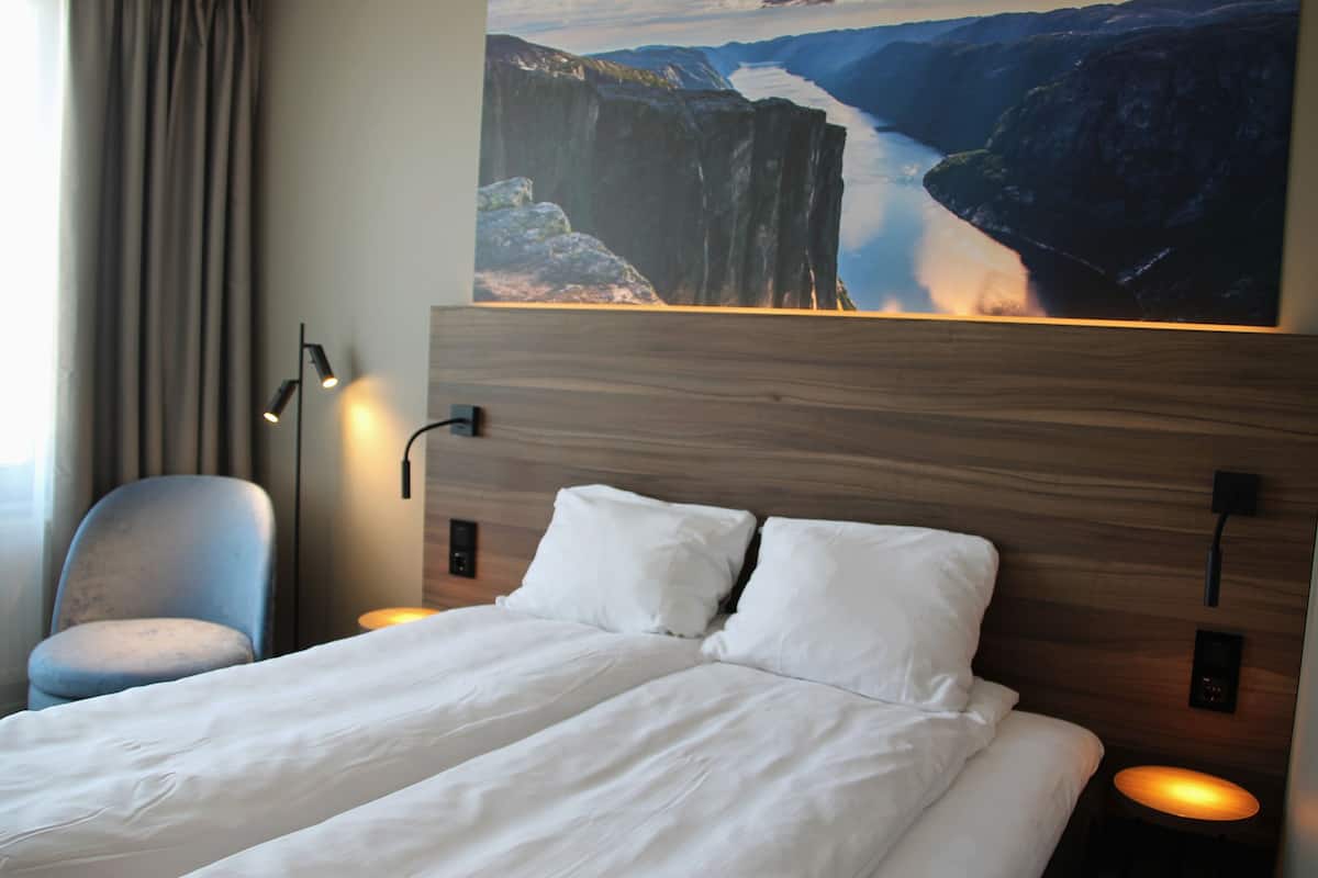 A hotel room with a large bed, two bedside lamps, a chair, and a painting of a canyon.