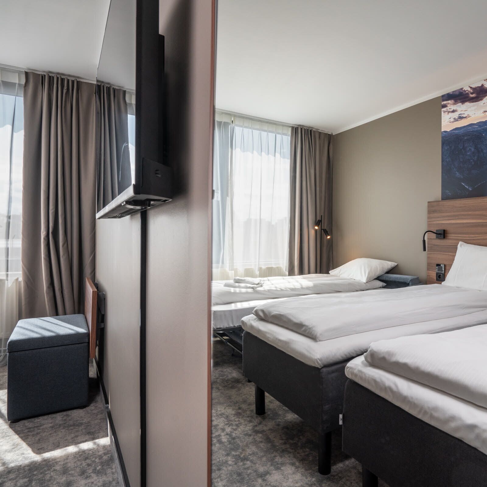 Et hotelværelse med to senge, et fjernsyn, et skrivebord og et billede på væggen.