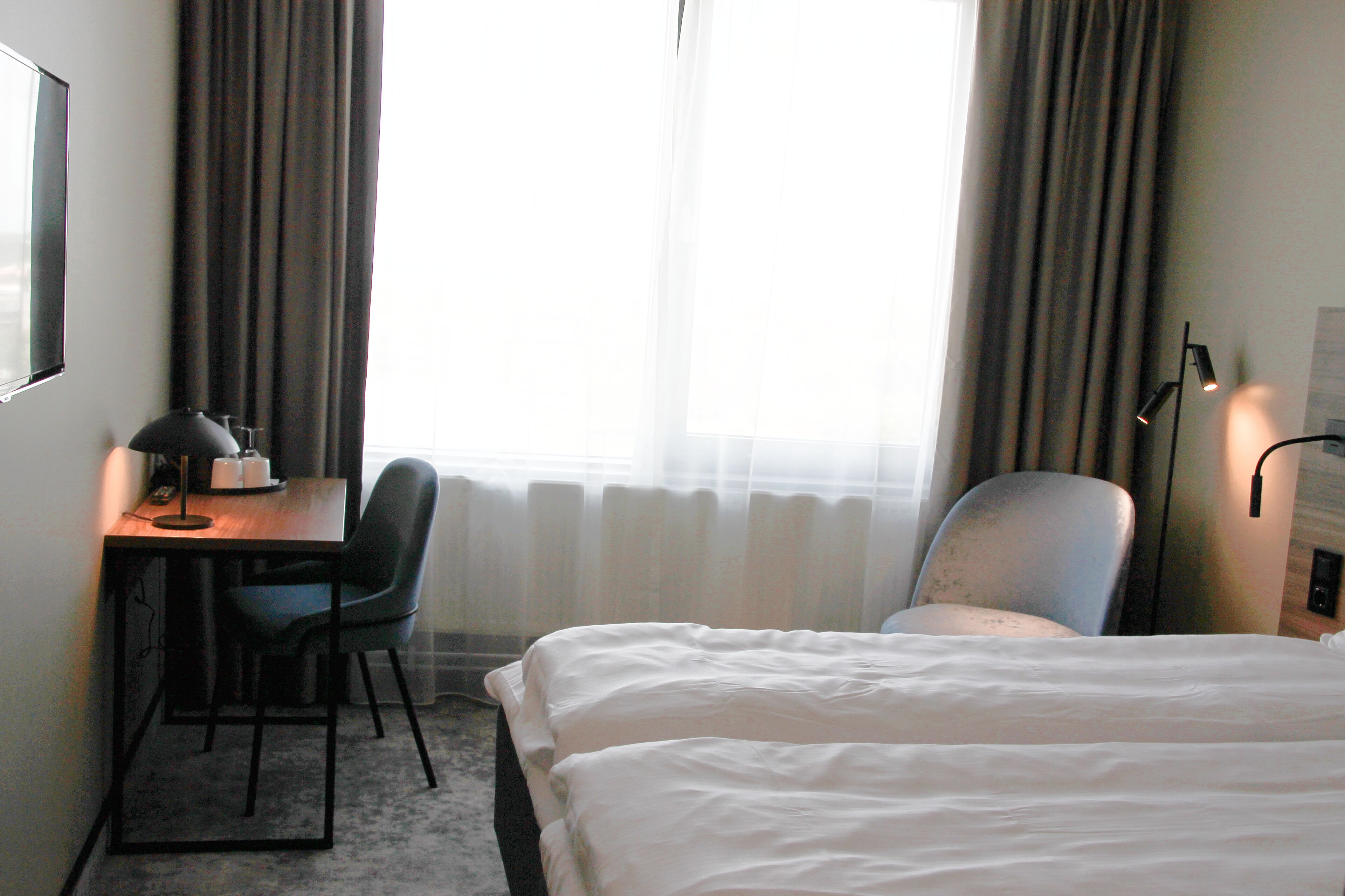 A hotel room with a bed, a desk, a chair, and a lamp.