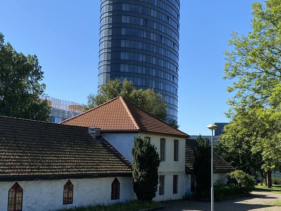 A traditional building with a tiled roof and a modern cylindrical structure in the background.