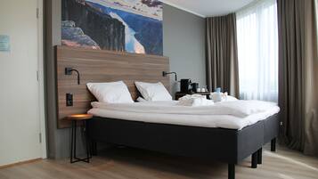 A modern hotel room with a large bed, a nightstand, a coffee maker, and a painting of a mountain landscape.