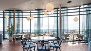 A modern dining area with round tables and chairs, large windows with a view of the city, and hanging spherical light fixtures. - Thon Hotel Stavanger Forum (Stavanger)