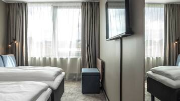 Habitación de hotel con dos camas, un espejo grande y vistas de la ciudad a través de cortinas de gasa.