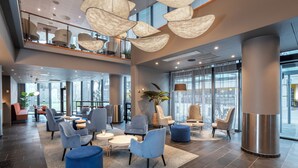 A spacious lobby with modern seating, large windows, and a high ceiling with unique lighting fixtures.