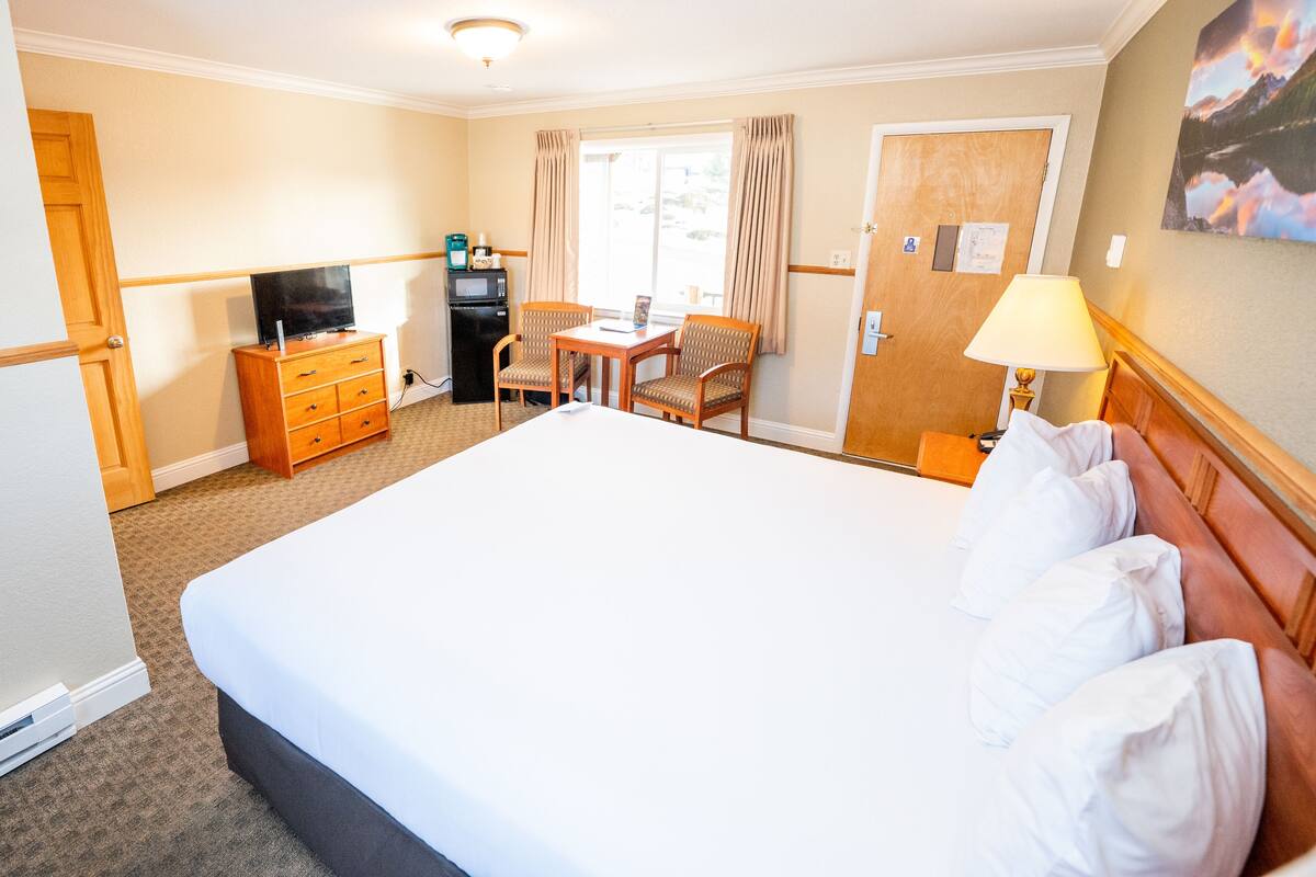 Une chambre d’hôtel avec un grand lit, un bureau avec deux chaises, une télévision et un minibar.