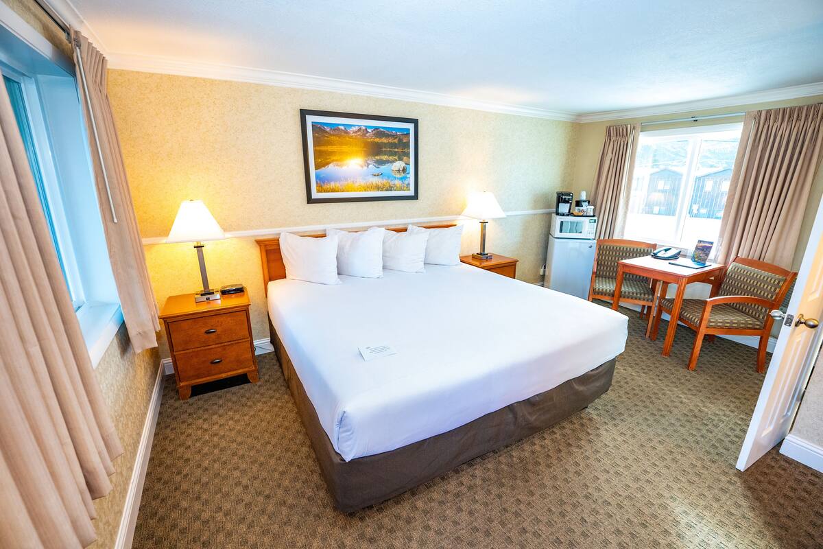 Une chambre d’hôtel avec un grand lit, deux tables de chevet, un bureau avec une chaise, une fenêtre avec des rideaux et un tableau au mur.
