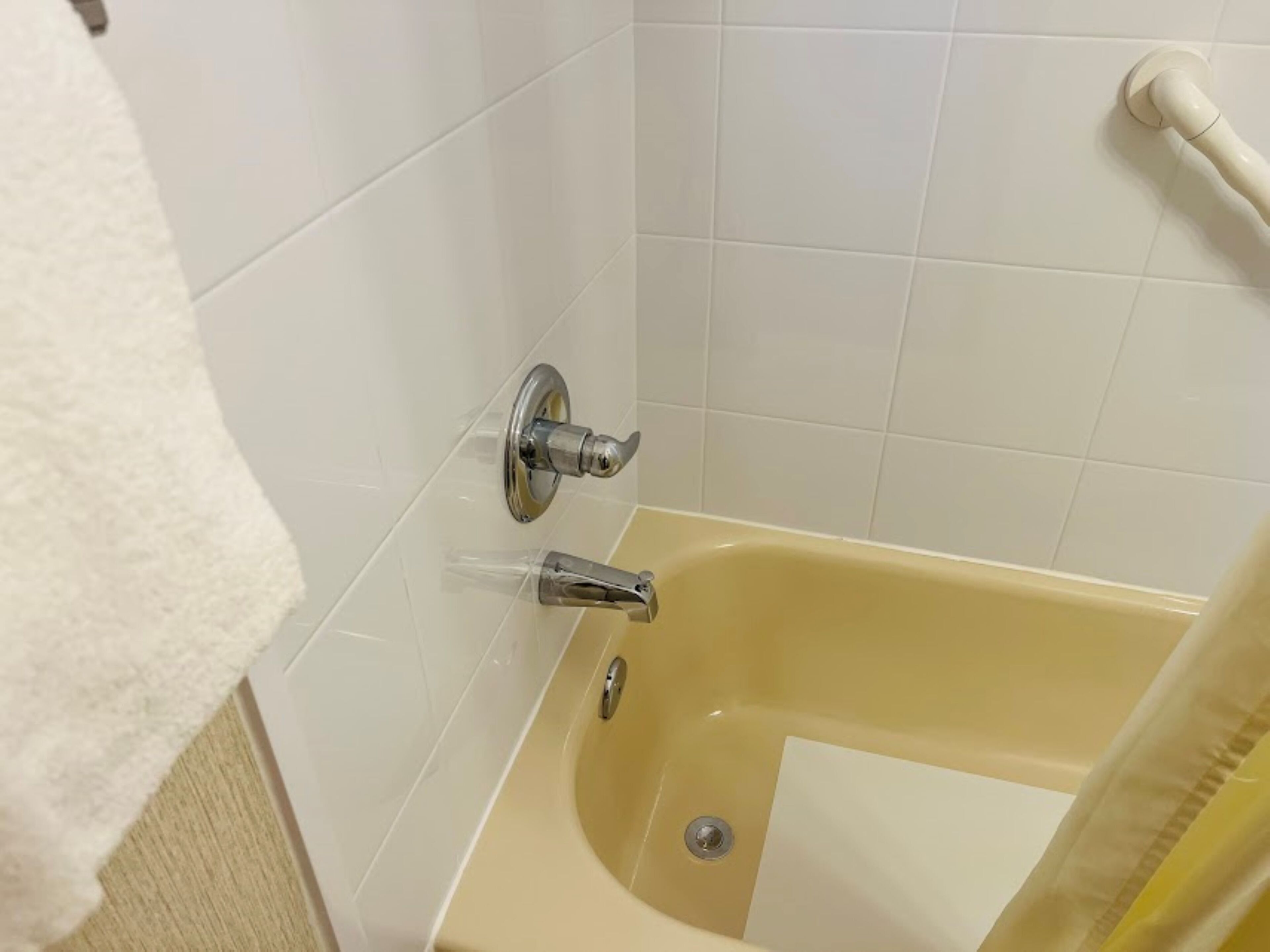 Un baño con bañera, paredes de azulejos blancos y una toalla blanca en el suelo.