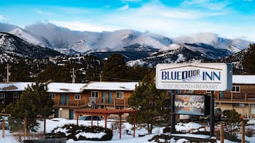 En skylt för värdshuset ”Blue Door Inn”, med en mindre skylt under som visar att det finns lediga rum, omgiven av snötäckta berg och en byggnad av trä.