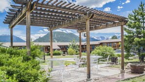 A wooden pergola with white metal chairs and tables, overlooking a mountain range. - Blue Door Inn (Estes Park)