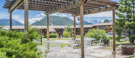 Une pergola en bois, agrémentée de chaises et de tables en métal blanc, offrant une vue sur une chaîne de montagnes.
