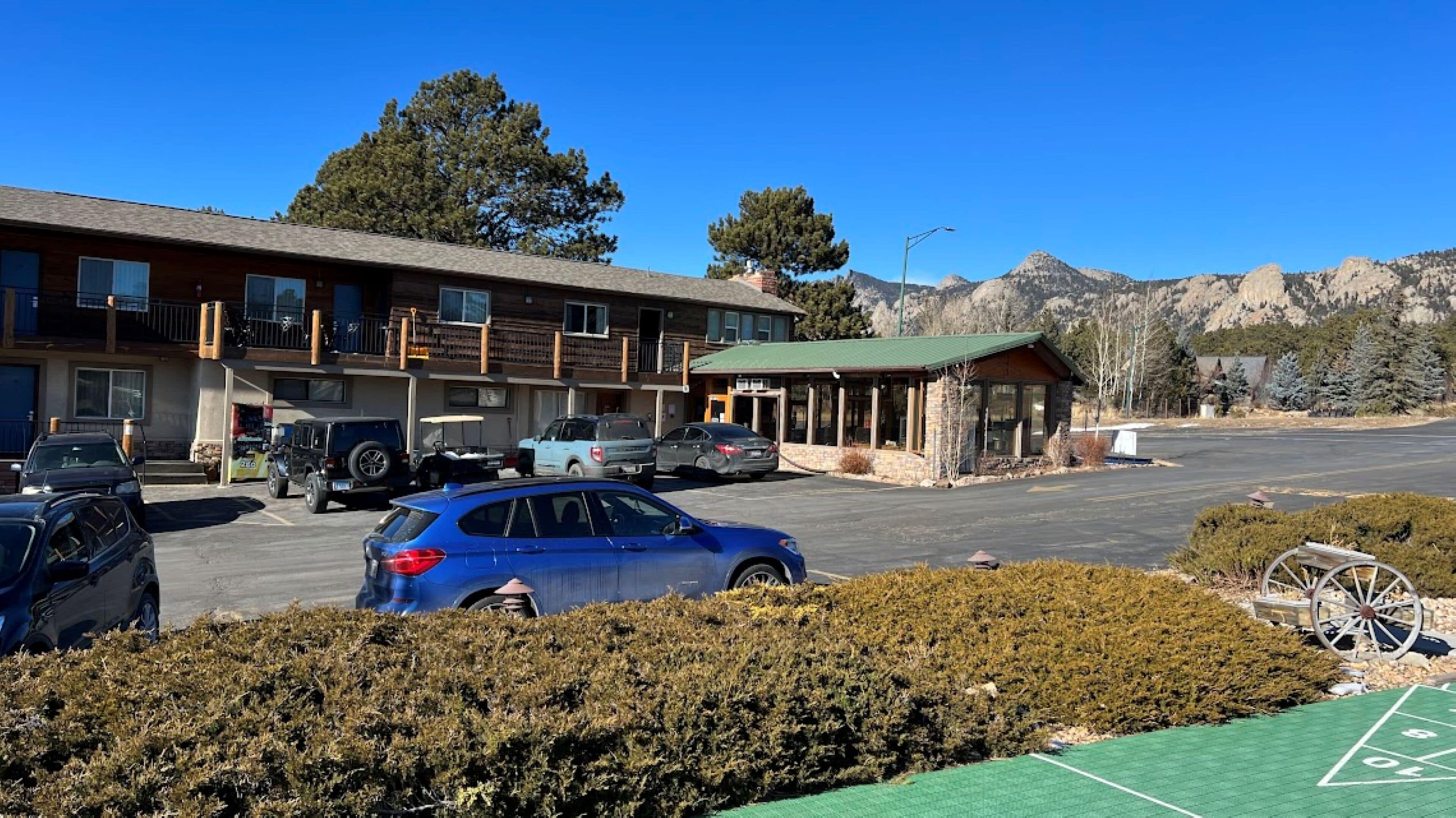 A motel with a parking lot, a small building with a green roof, and mountains in the background.