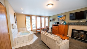 A spacious living room with a large sofa, a fireplace, a television mounted on the wall, and a hot tub in the corner. - Blue Door Inn (Estes Park)
