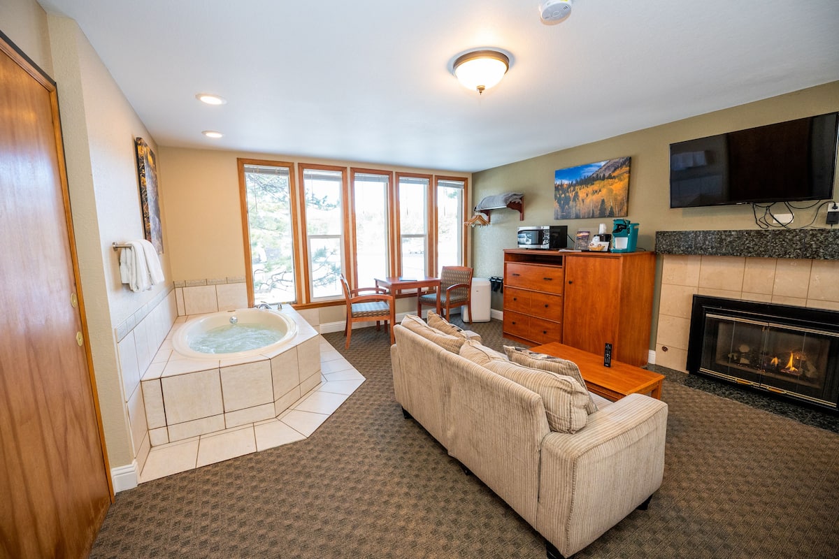 Un vaste salon comprenant un grand canapé, une cheminée, un téléviseur fixé au mur et un jacuzzi installé dans un coin.