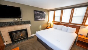 A hotel room with a large bed, a fireplace, a television, and a window with blinds. - Blue Door Inn (Estes Park)