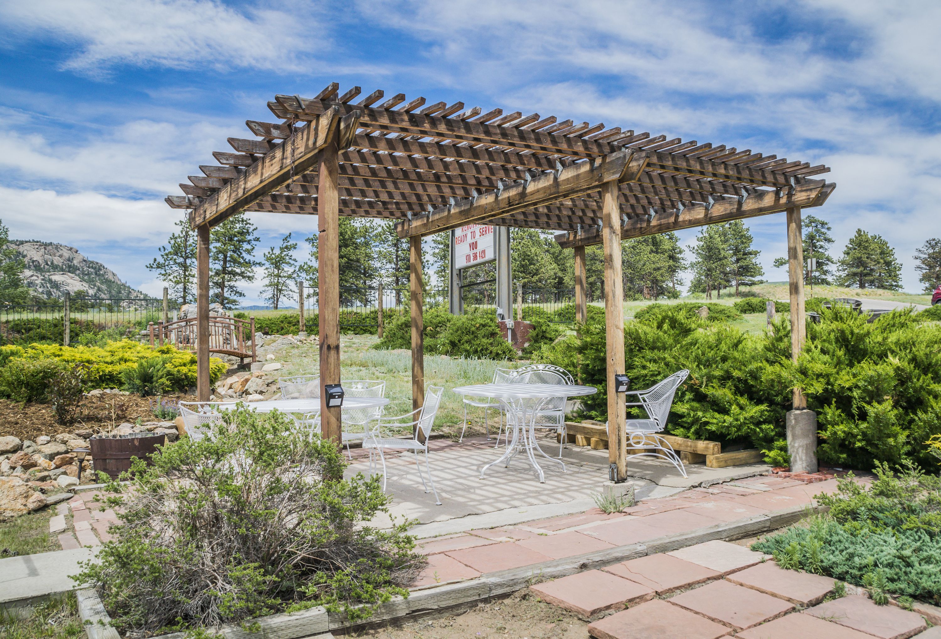 Una pérgola de madera con mesa y sillas debajo, rodeada de vegetación y un paisaje montañoso.