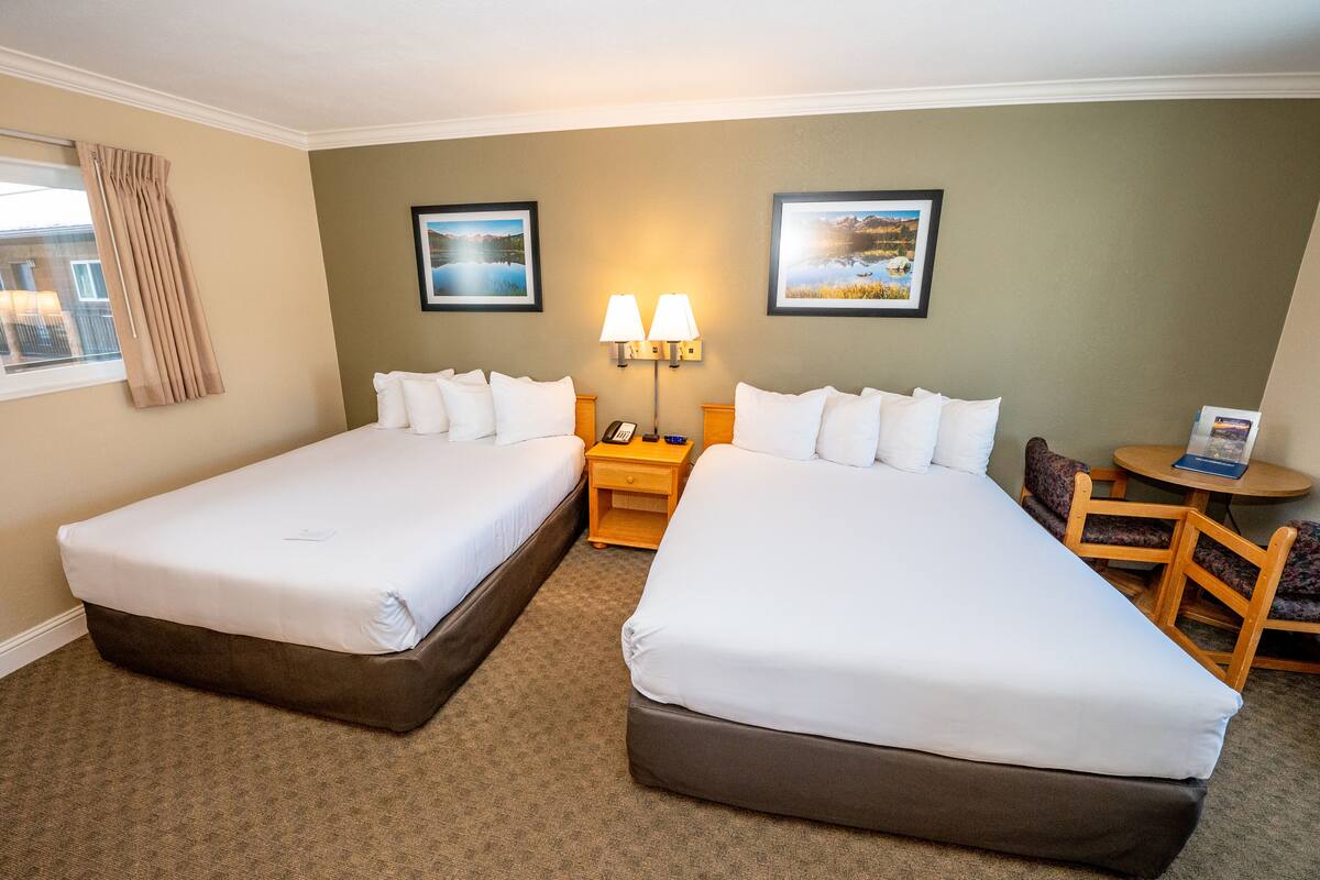 Une chambre d’hôtel avec deux lits simples, une petite table, une chaise, une lampe et deux tableaux encadrés au mur.