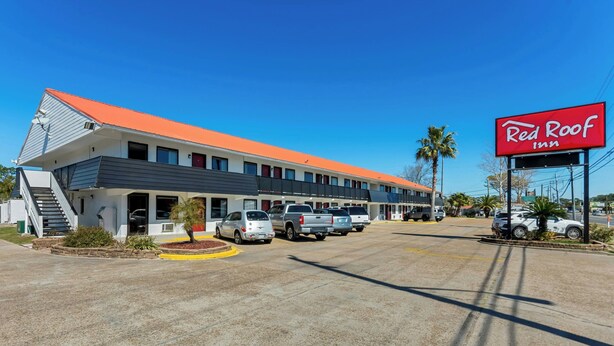 A Red Roof Inn with a red roof, multiple parking spaces, and a clear blue sky.
