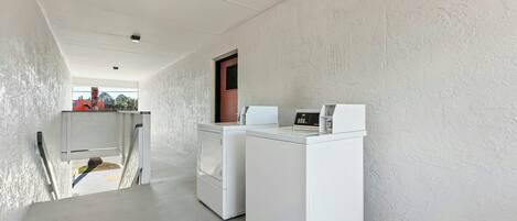 A laundry area with two white washing machines and a dryer, a small window with a view, and a door leading to another room.