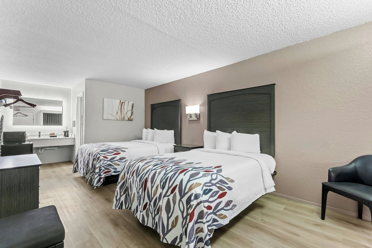 Ein Hotelzimmer mit zwei Betten, einem Schreibtisch, einem Stuhl und einem Kleiderschrank.