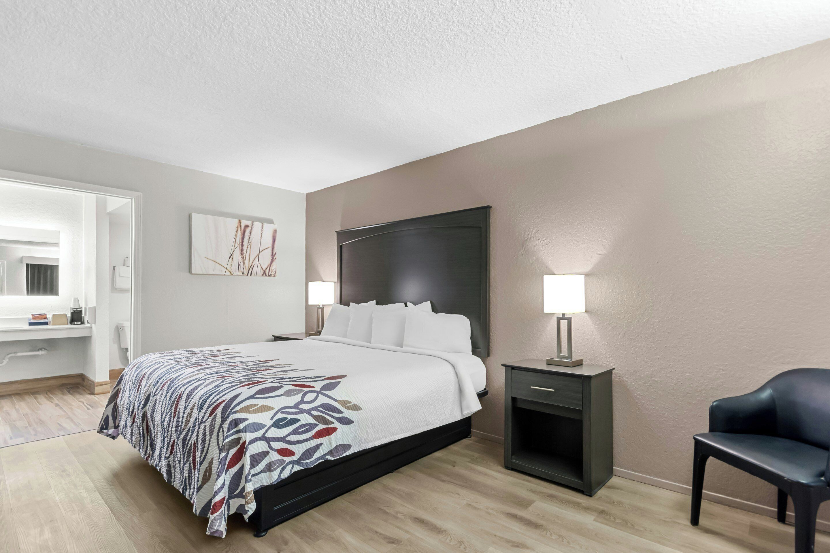 A hotel room with a bed, bedside tables, a chair, and a door leading to a bathroom.