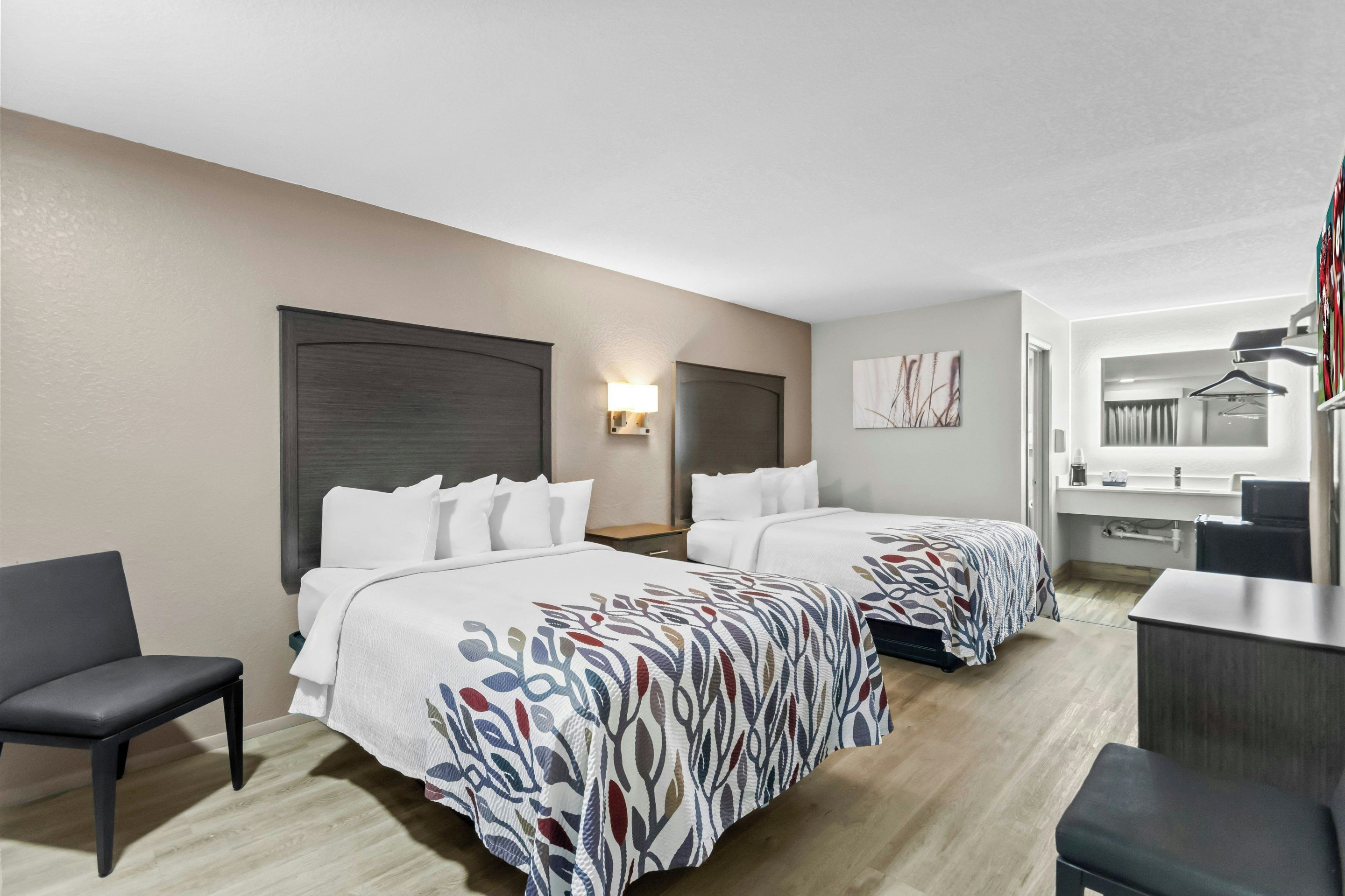 Habitación de hotel con dos camas, un escritorio, una silla y un perchero.