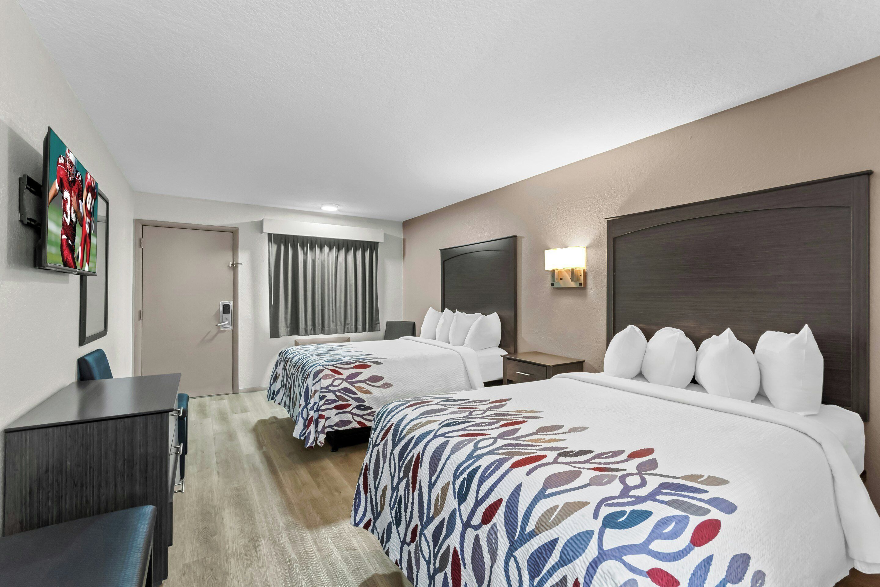 Una habitación de hotel con dos camas, un escritorio, un televisor y una ventana con cortinas.