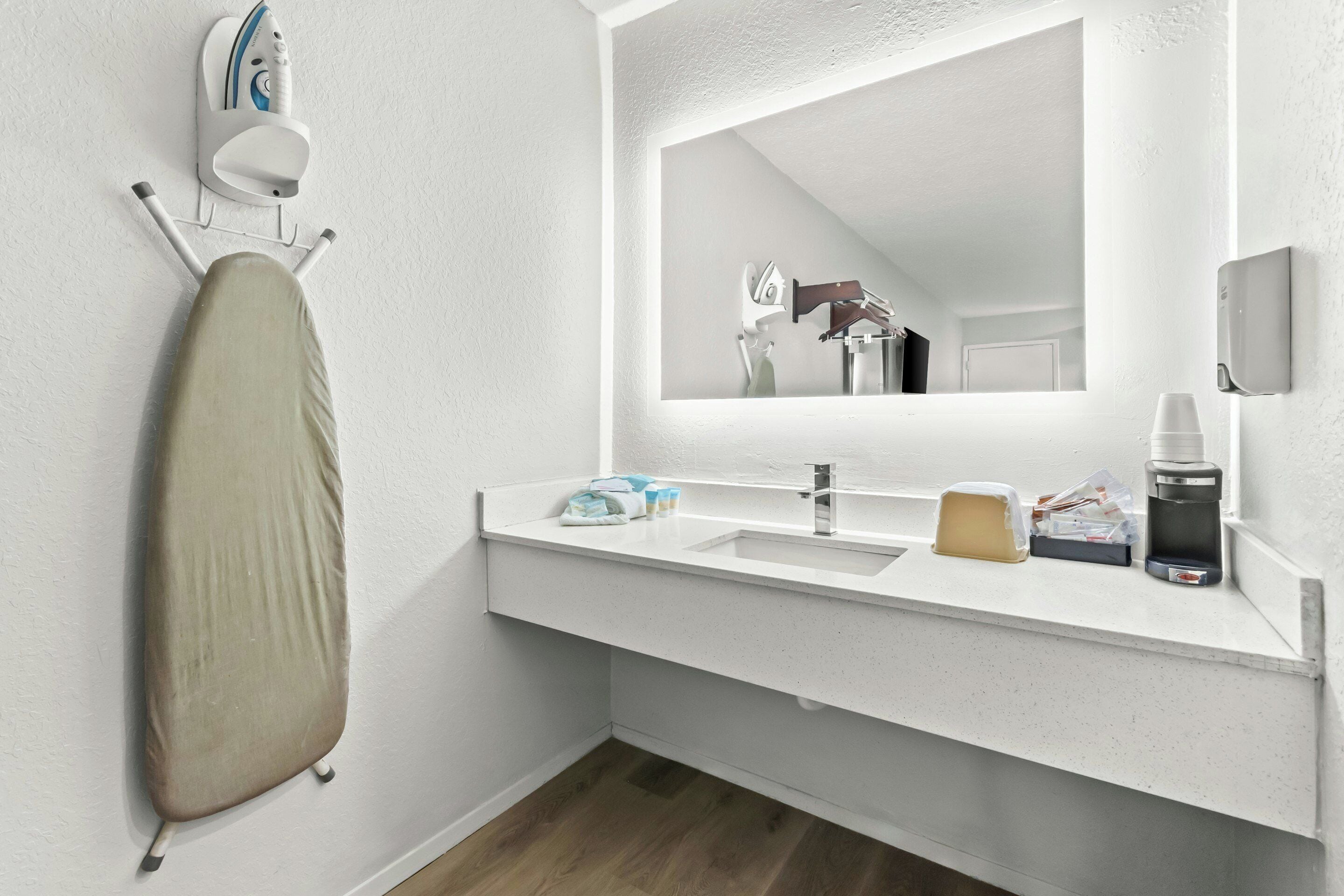 Un baño moderno con un espejo grande, un lavamanos y una tabla de planchar.