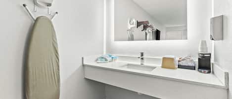 Un baño moderno con un espejo grande, un lavamanos y una tabla de planchar.