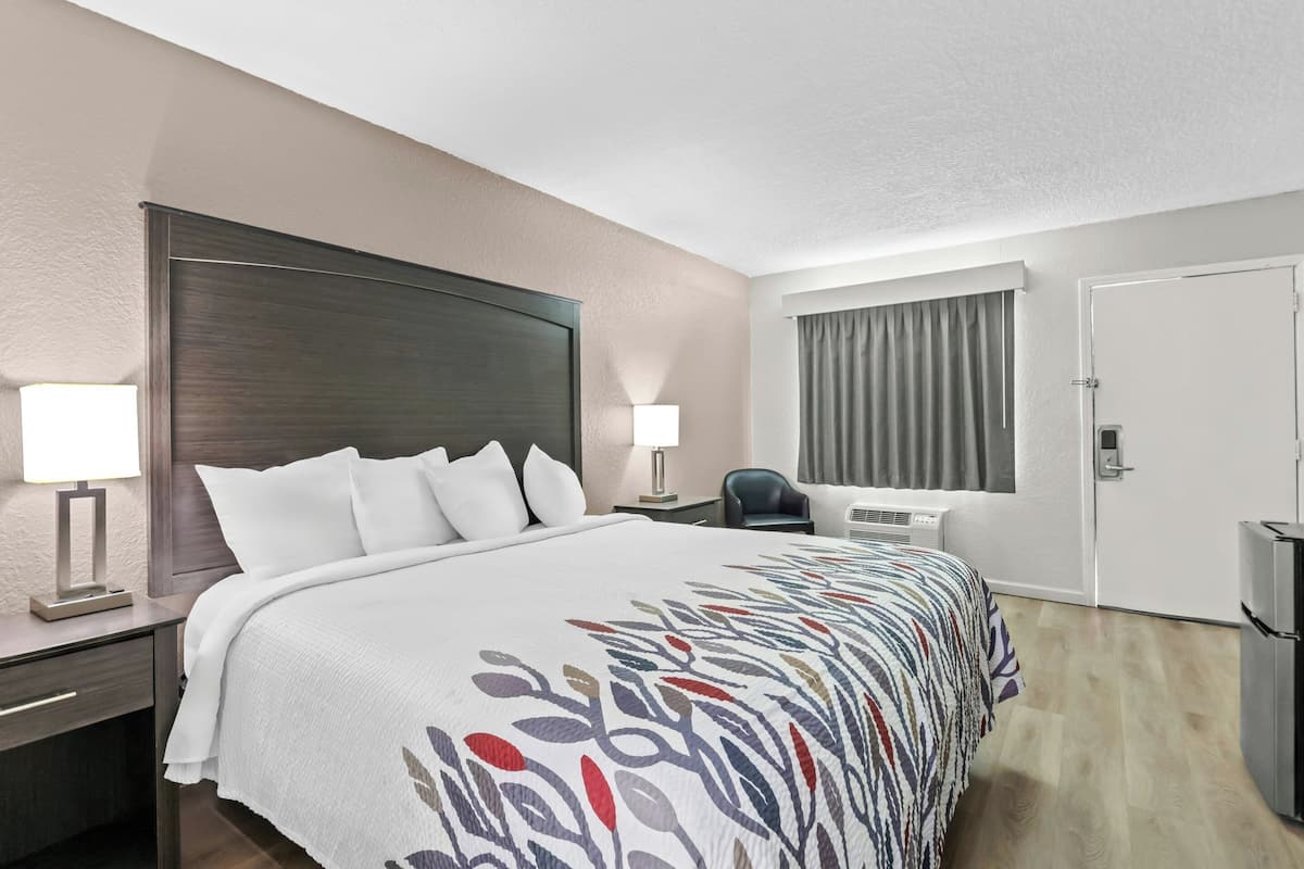 Ein Hotelzimmer mit einem großen Bett, Nachttischlampen, einem Schreibtisch, einem Stuhl, einer Klimaanlage und einer Tür.