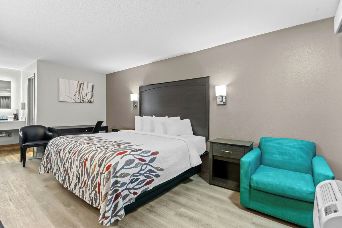 A hotel room with a bed, a desk, a chair, and a small table.