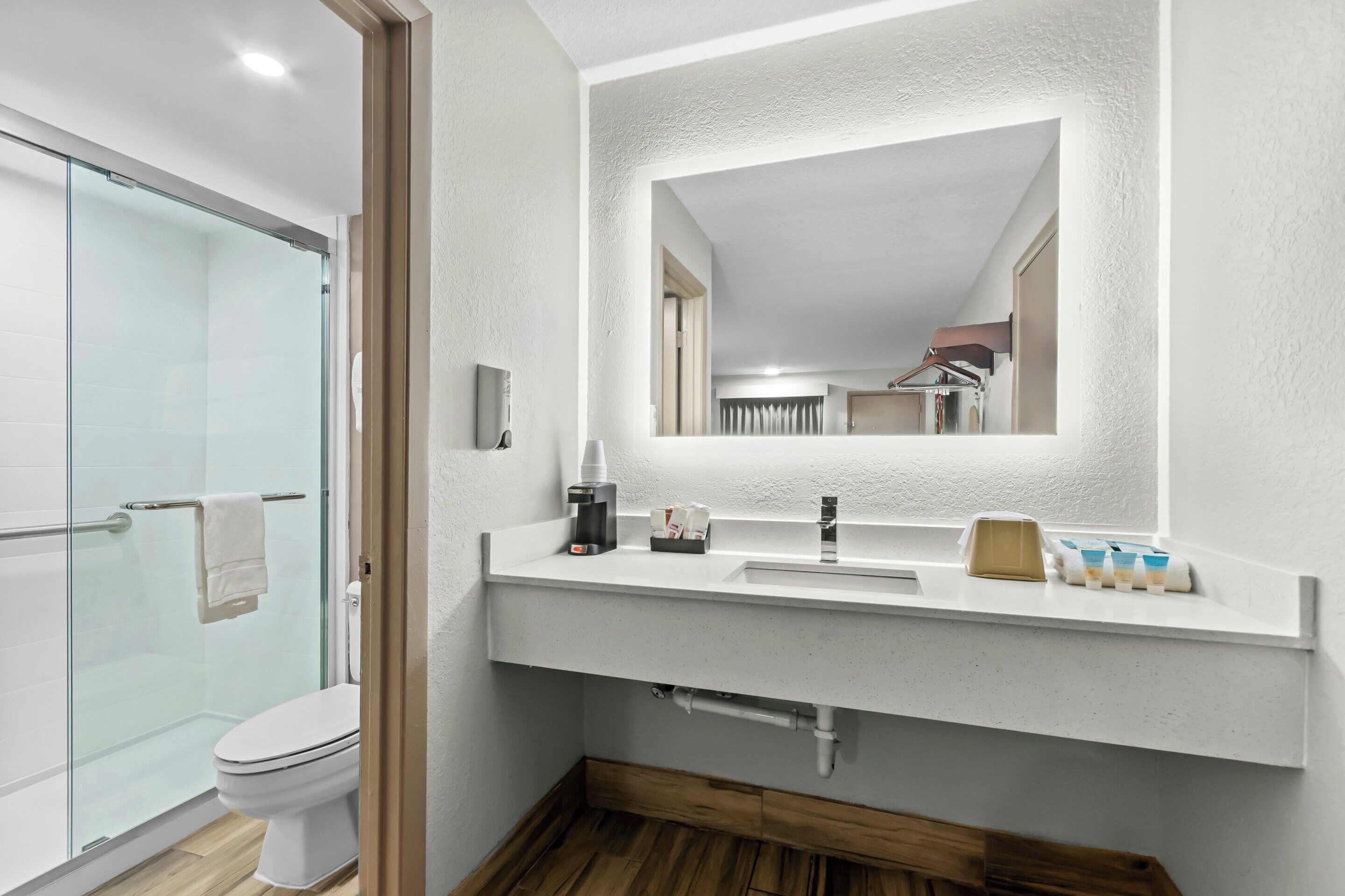 Un baño moderno con cabina de ducha de vidrio, un lavabo blanco con espejo y suelo de madera.