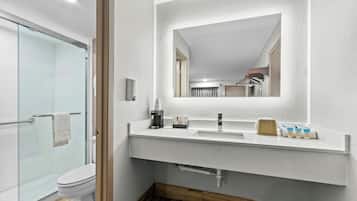Un baño moderno con cabina de ducha de vidrio, un lavabo blanco con espejo y suelo de madera.