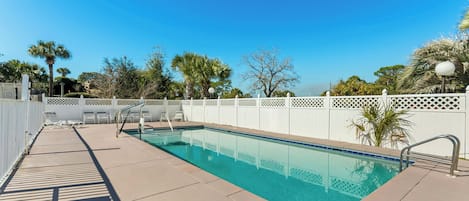 A rectangular swimming pool with clear blue water, surrounded by a white fence and palm trees.
