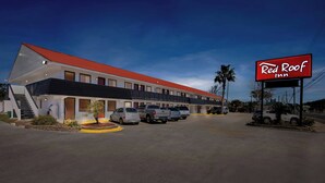 A Red Roof Inn with a red roof, multiple parking spaces, and a clear sky.