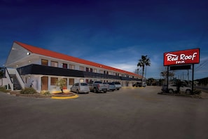 A Red Roof Inn with a red roof, multiple parking spaces, and a clear sky.
