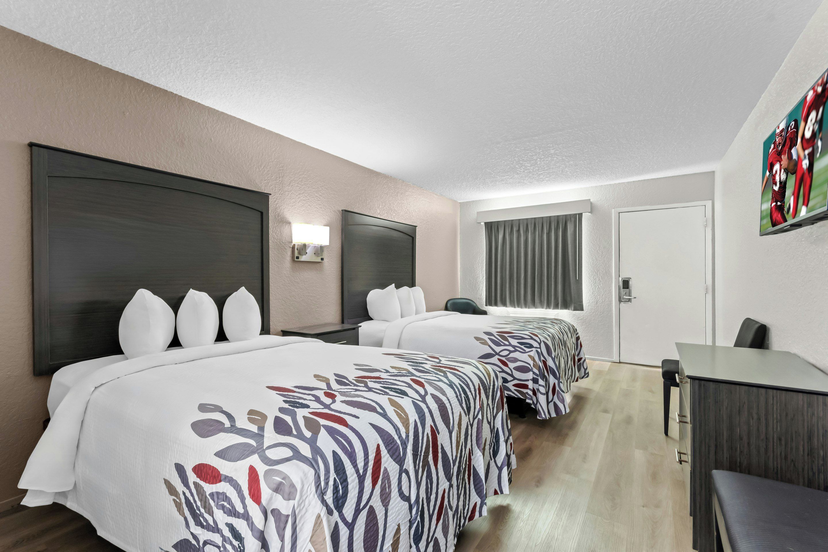 A hotel room with two beds, a desk, and a television.