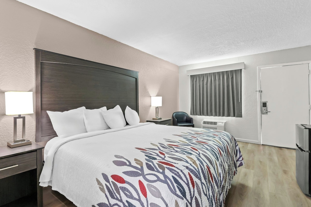Habitación de hotel con una cama grande, lámparas de noche, escritorio, una silla, equipo de aire acondicionado y una puerta.