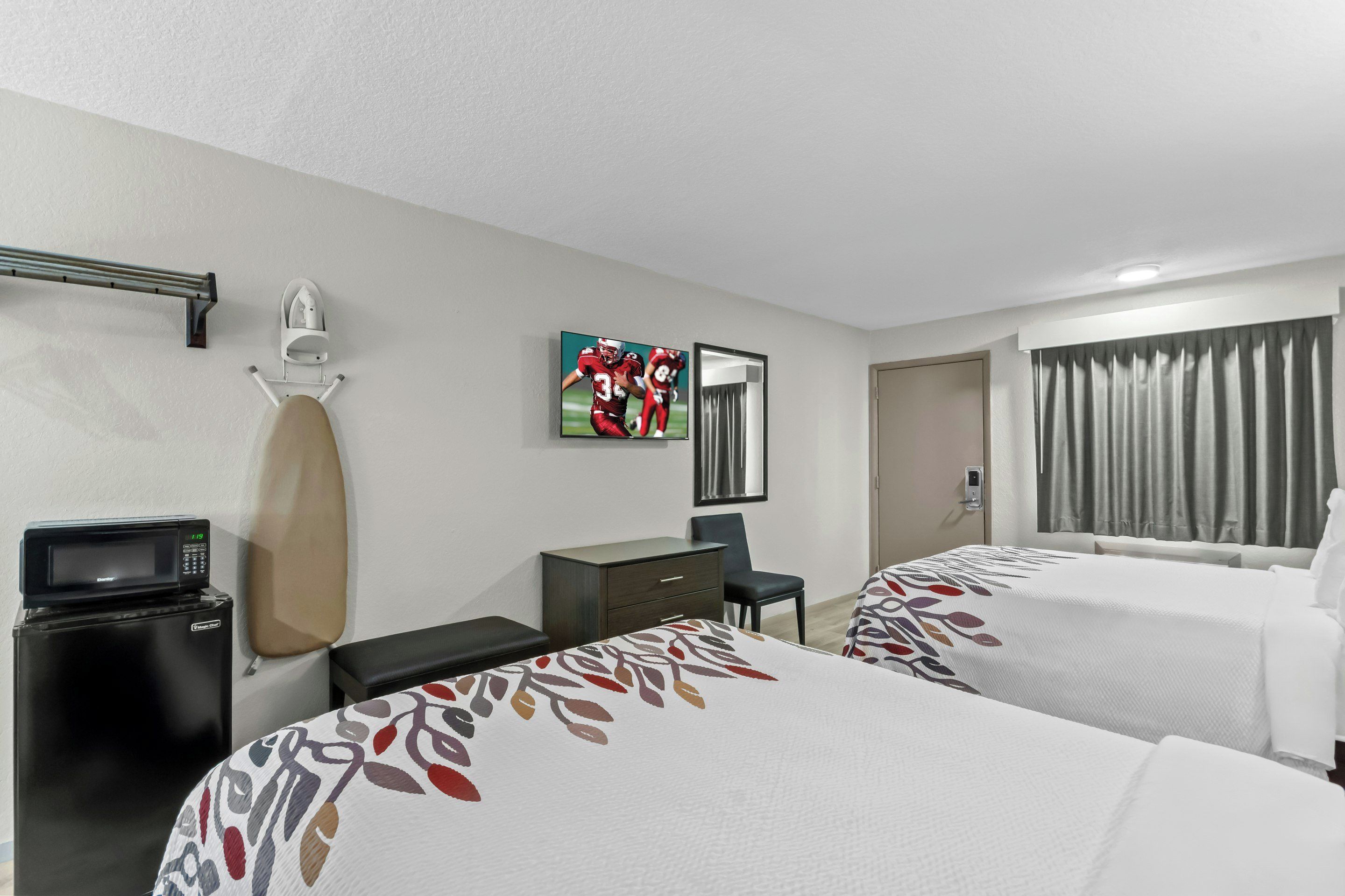 A hotel room with two beds, a desk, a chair, a microwave, and a TV.