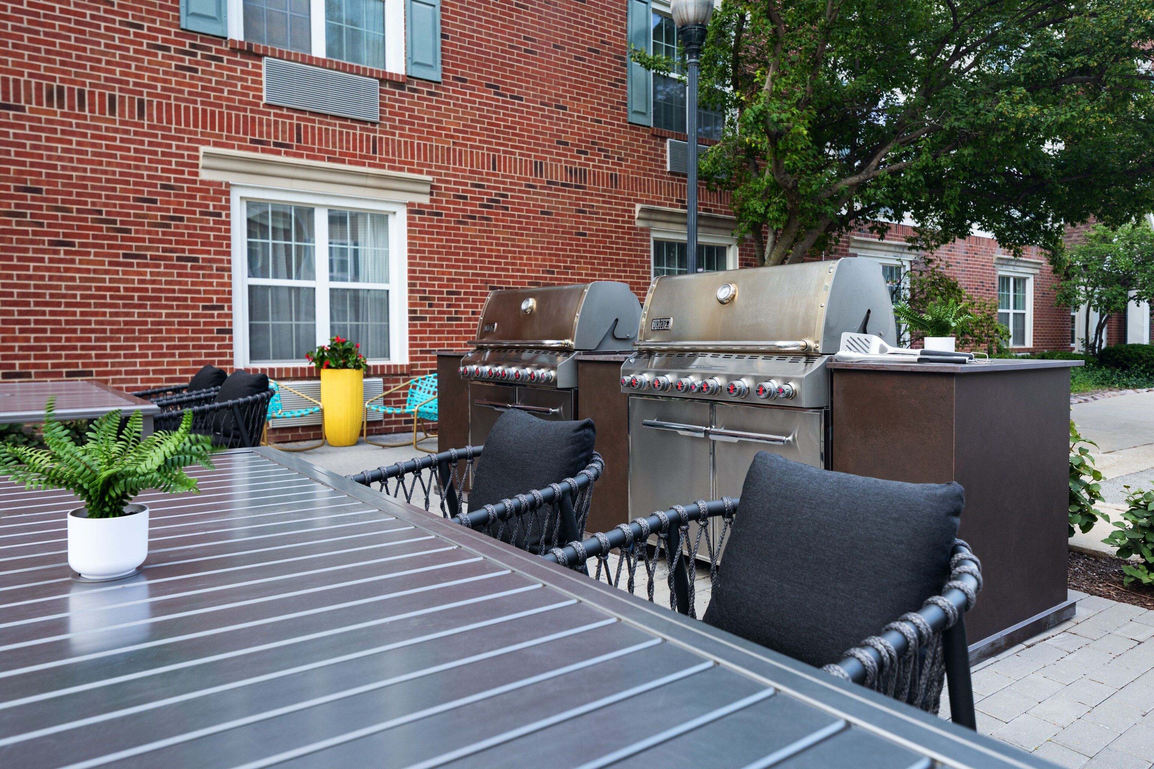 Un patio al aire libre con una parrilla, sillas de mimbre y una planta en maceta.