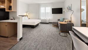 A hotel room with a bed, a desk, a sofa, a TV, and a large mirror. - TownePlace Suites by Marriott Chicago Lombard (Lombard)