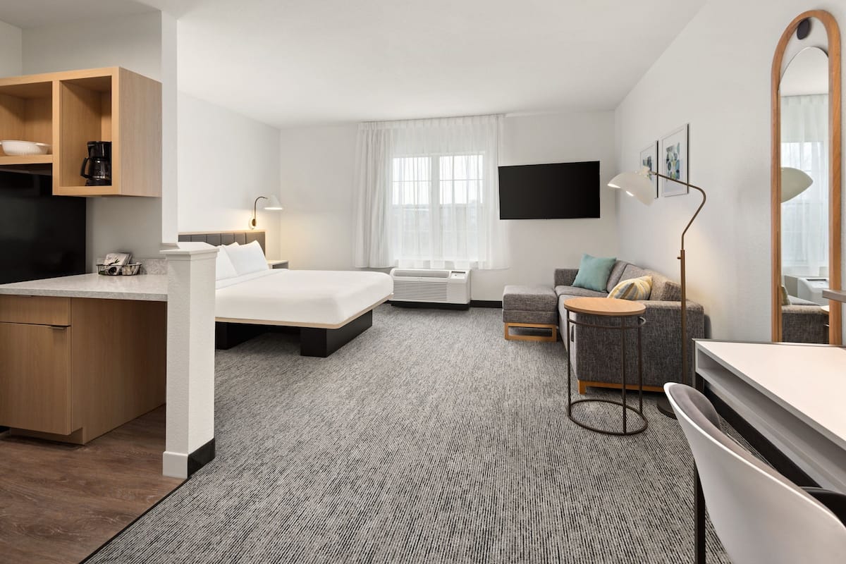 A hotel room with a bed, a desk, a sofa, a TV, and a large mirror.