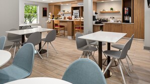 A modern dining area with wooden flooring, grey upholstered chairs, and white tables. - TownePlace Suites by Marriott Chicago Lombard (Lombard)