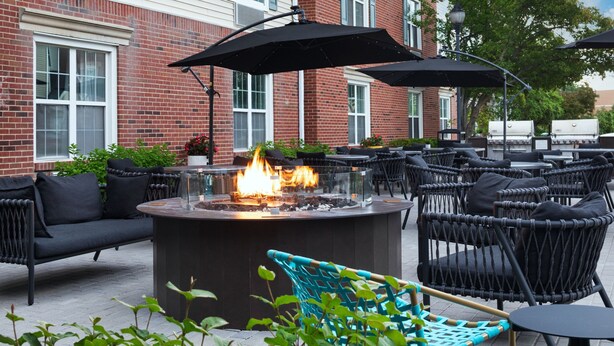 An outdoor patio with a fire pit, wicker furniture, and a brick building in the background. - TownePlace Suites by Marriott Chicago Lombard (Lombard)