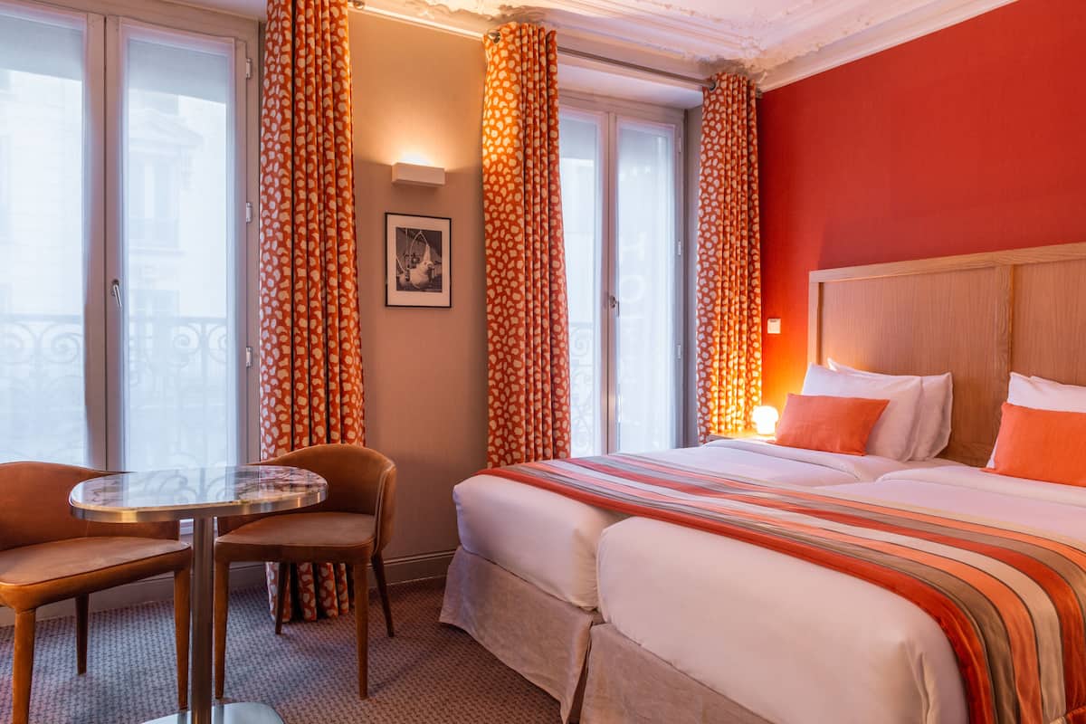 Habitación de hotel con cama, dos sillas, una mesita y ventana con cortinas.