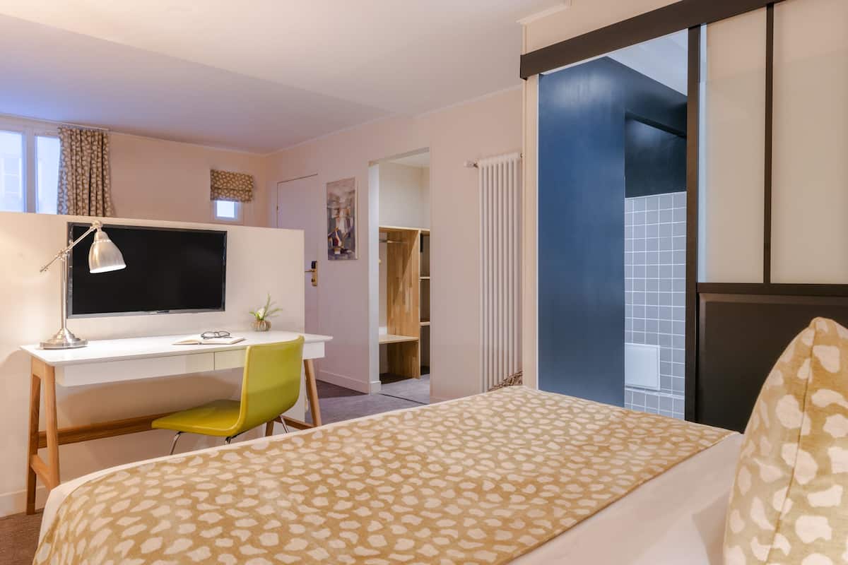Habitación de hotel con cama, escritorio con computadora, una silla, televisor y vista a una pared azul y una ventana.