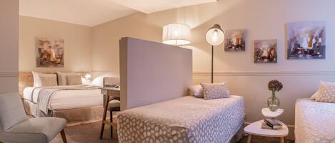 A hotel room with two beds, a desk, a chair, a lamp, and artwork on the walls.