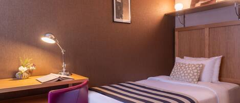 Una habitación de hotel con una cama, un escritorio con lámpara, una silla y una pequeña mesa con un jarrón de flores.