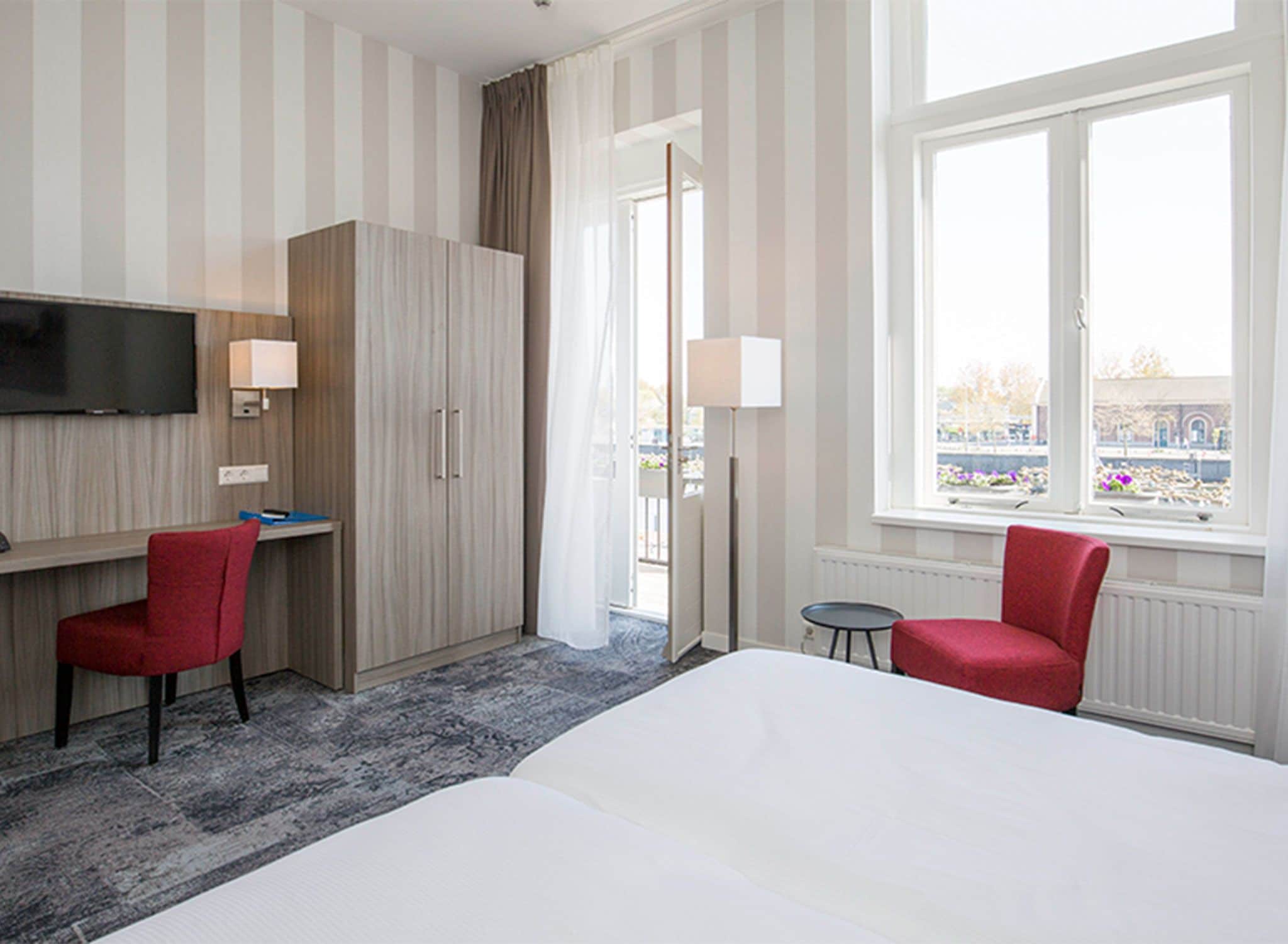 A hotel room with a bed, a desk, a TV, and a window with a view.