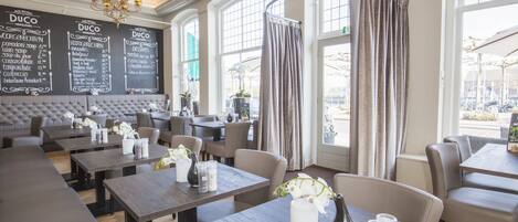 Un restaurante con mesas altas, asientos acolchados y un menú en una pizarra.
